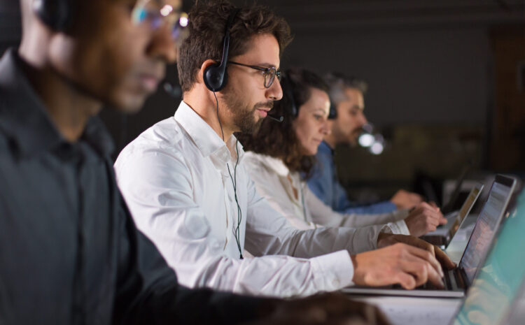 Side view of confident call center operator talking with client. Caucasian young man in eyeglasses typing on laptop while serving client. Call center concept